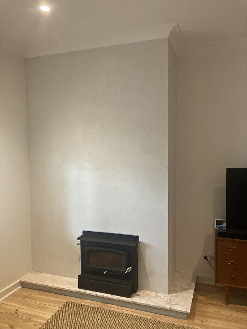 A full-height textured plaster chimney wall with a black wood heater on a stone hearth