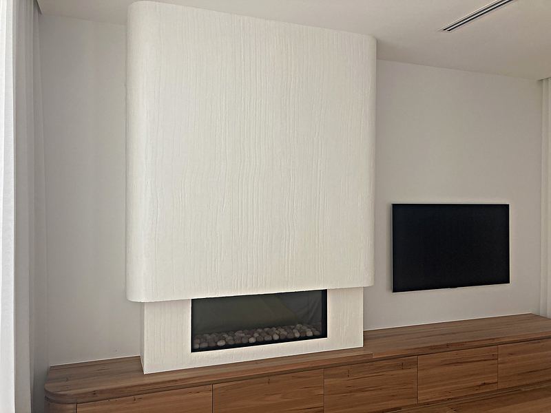 A curved white fireplace feature wall in hand-trowelled plaster above a gas fireplace and timber cabinetry