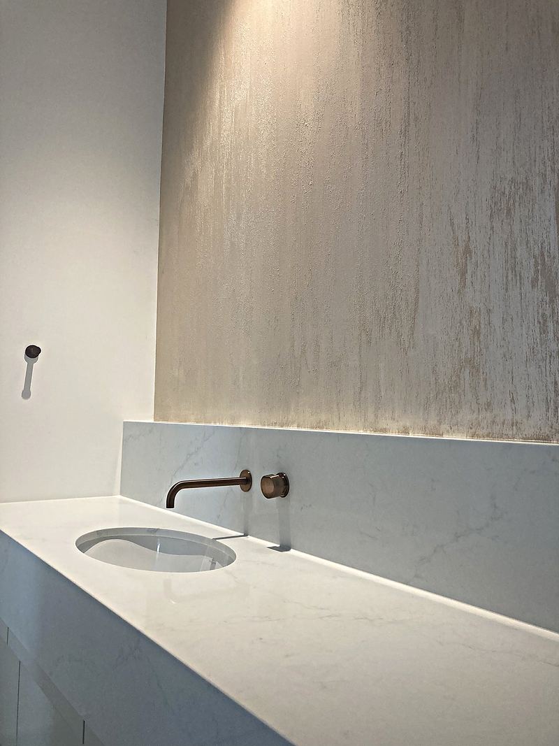 A softly lit wall of hand-trowelled Venetian plaster above a marble vanity with a brushed copper tap, finished by Ed