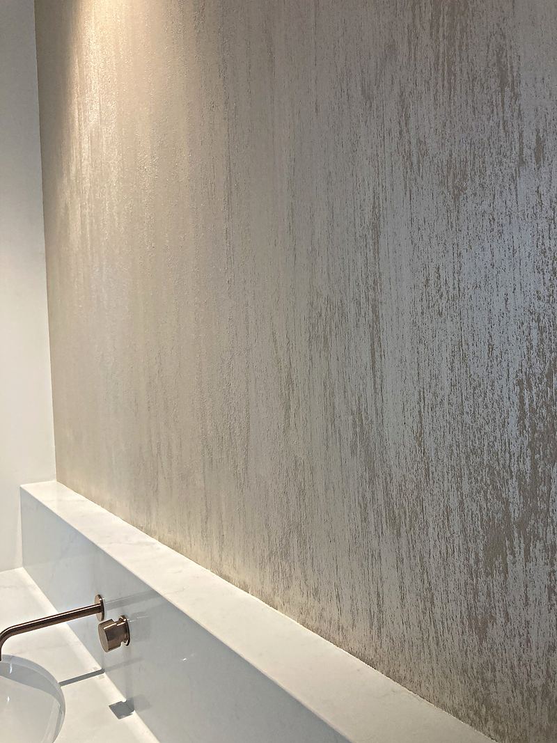 Hand-trowelled Venetian plaster wall glowing under a strip light above a marble vanity
