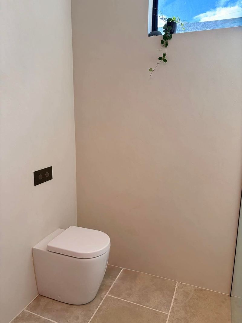 A powder room finished in soft, seamless plaster with a back-to-wall toilet