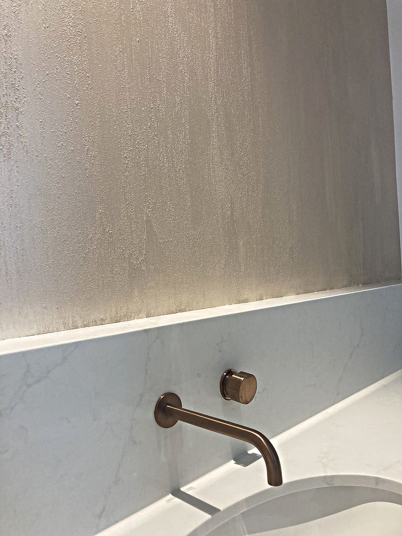 Hand-trowelled plaster catching the light above a marble benchtop and copper tap